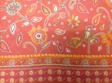 Voile-achtige stof met bloem en rand in oranje tinten met zilverglans elementen. Licht doorschijnend. Mooi voor blouse, tuniek, shawl of bovenlaag van een rokje